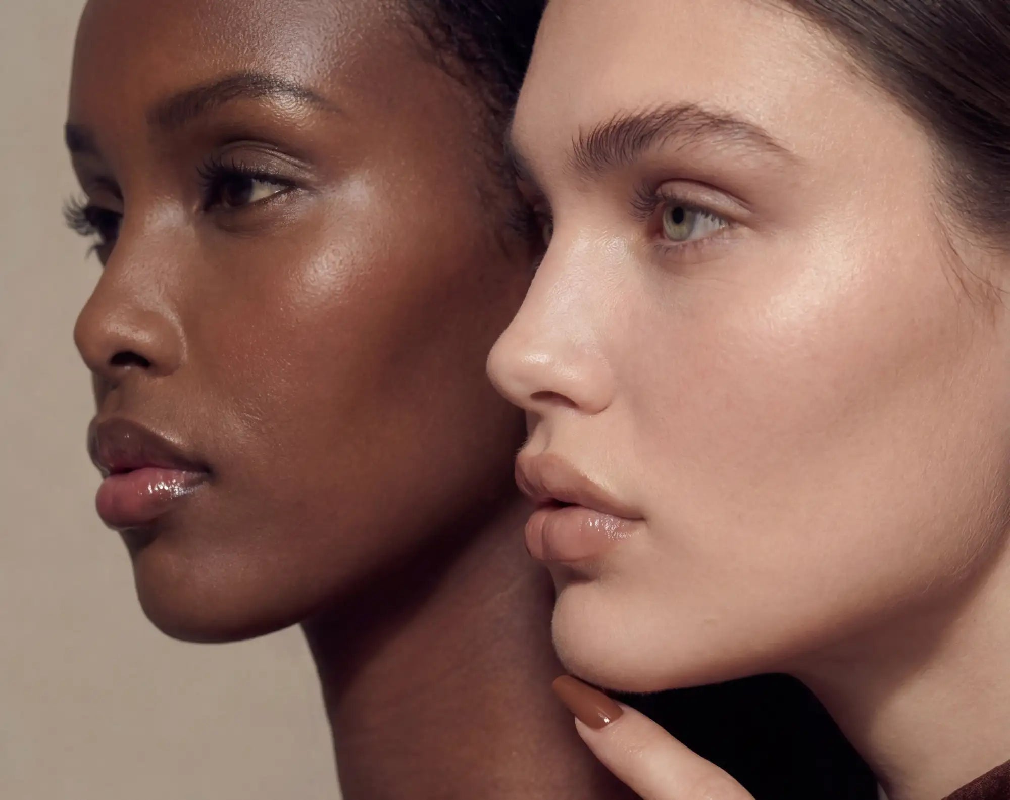 Ett närbildsporträtt av två kvinnor med slät, glödande hud och glansiga läppar.
